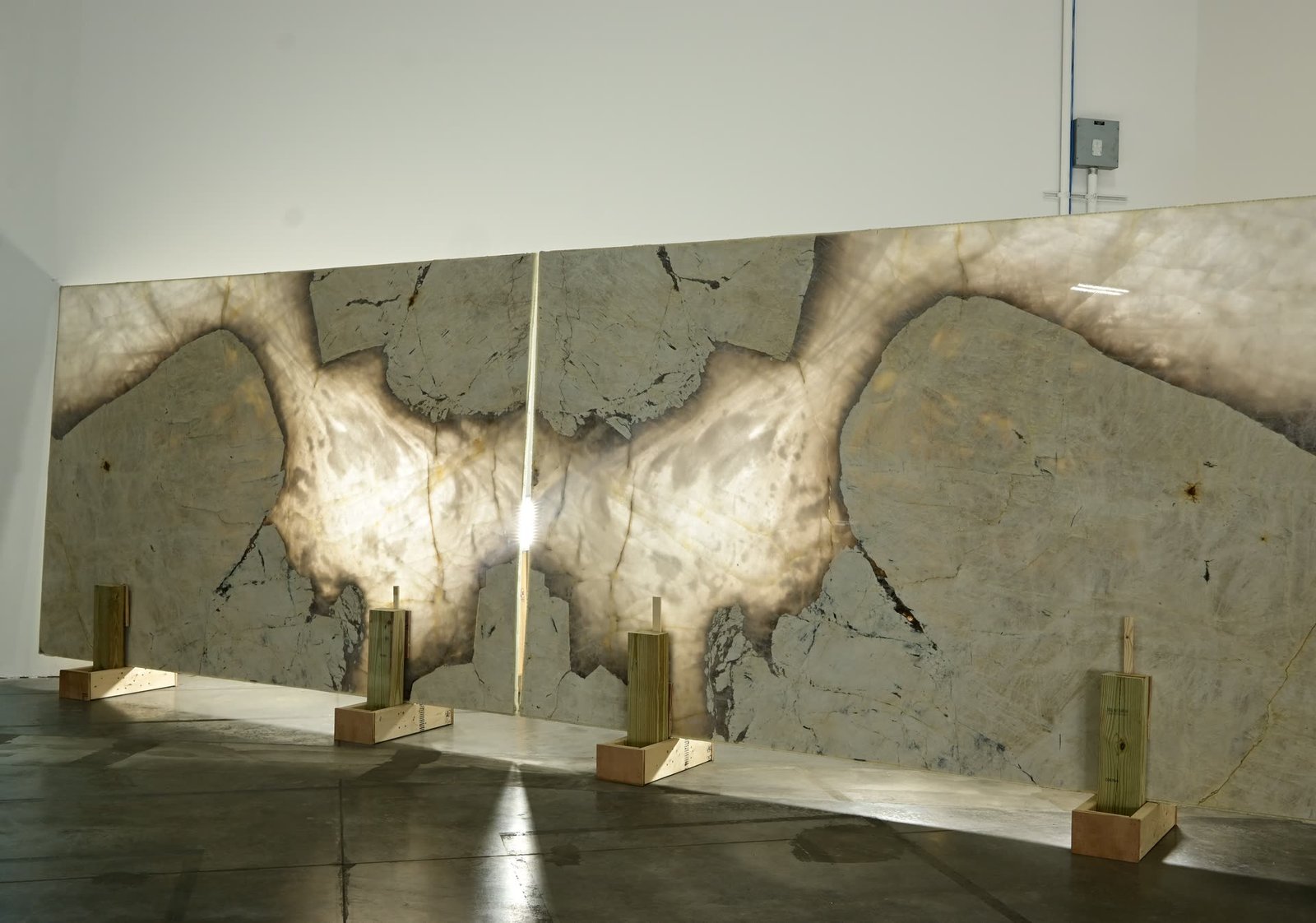 Two mirrored stone panels lit from behind, standing on timber supports against a showroom wall, the pattern forming a symmetrical figure across the join.