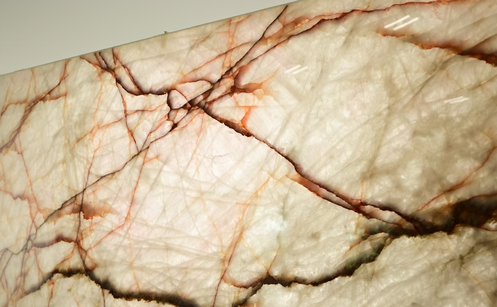 Close view of a translucent pale stone surface with fine orange and brown veins running across it.