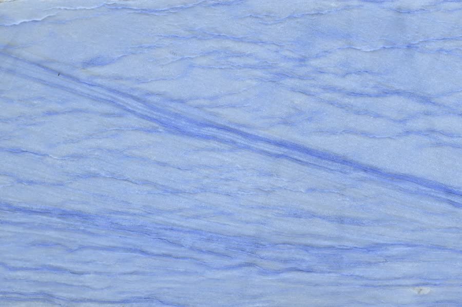 Close-up of a polished stone surface in soft cornflower blue and white, with fine horizontal layering and a pronounced deeper blue diagonal vein running from the upper left toward the right edge.