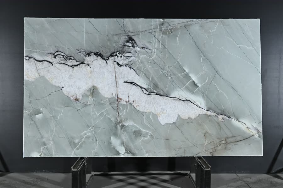 A full slab of pale green stone displayed upright on a black backdrop, a broad band of white crystalline veining edged in black running diagonally across it, resting on a dark metal A-frame stand.