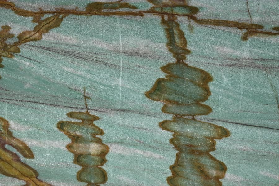 Macro view of a polished stone surface in soft sea green with fine pale striations, marked by two vertical columns of stacked lens-shaped amber and olive formations outlined in rust brown, with more branching veins along the top edge.