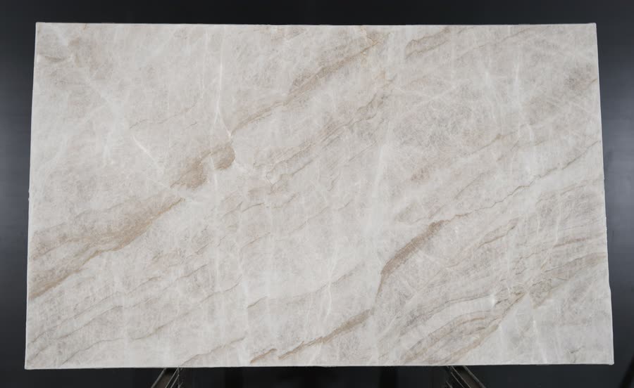 A full Tajmahal slab on a metal A-frame against a black studio backdrop, pale with soft beige and tan diagonal veining.