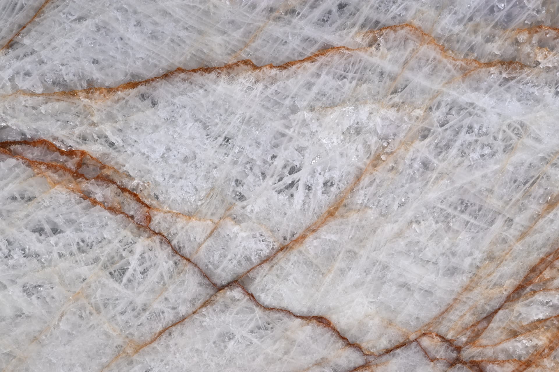 Rosso Crystallo, close: icy white and pale grey crystalline stone crossed by branching rust-orange and amber veins.