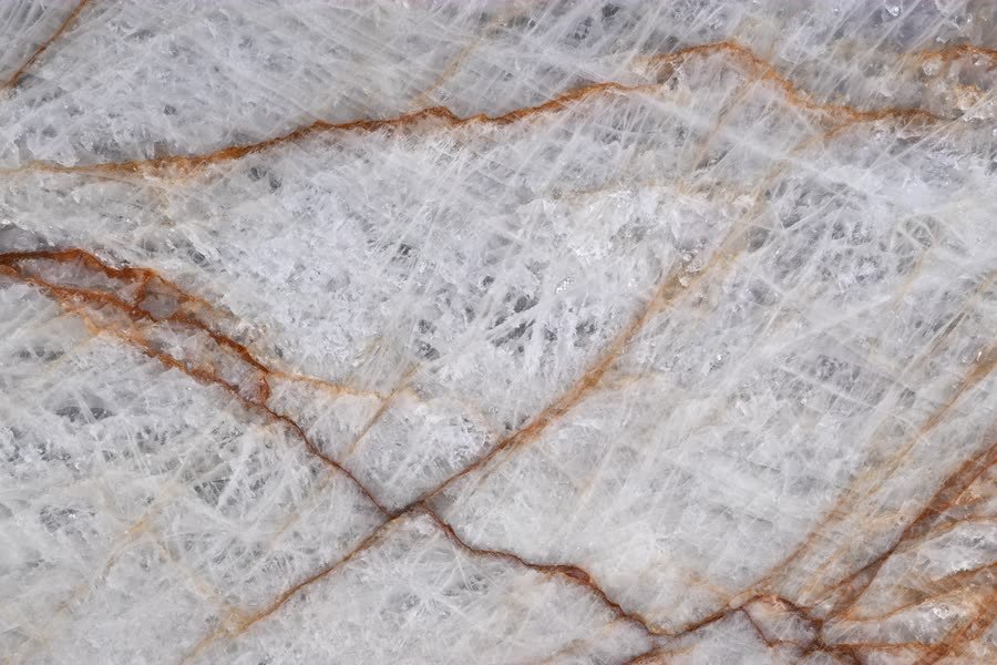 Rosso Crystallo — close view of the stone surface. White crystal crossed by rust-red and amber veining.