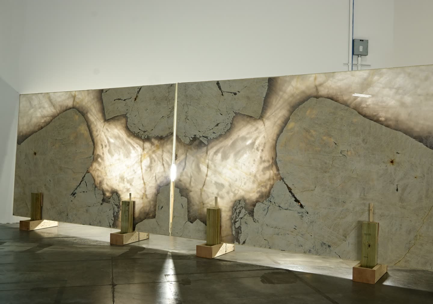 Two mirrored stone panels lit from behind, standing on timber supports against a showroom wall, the pattern forming a symmetrical figure across the join.